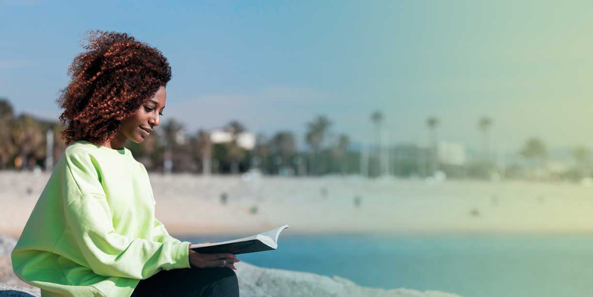 Lady with dark curly hair reading by the lake